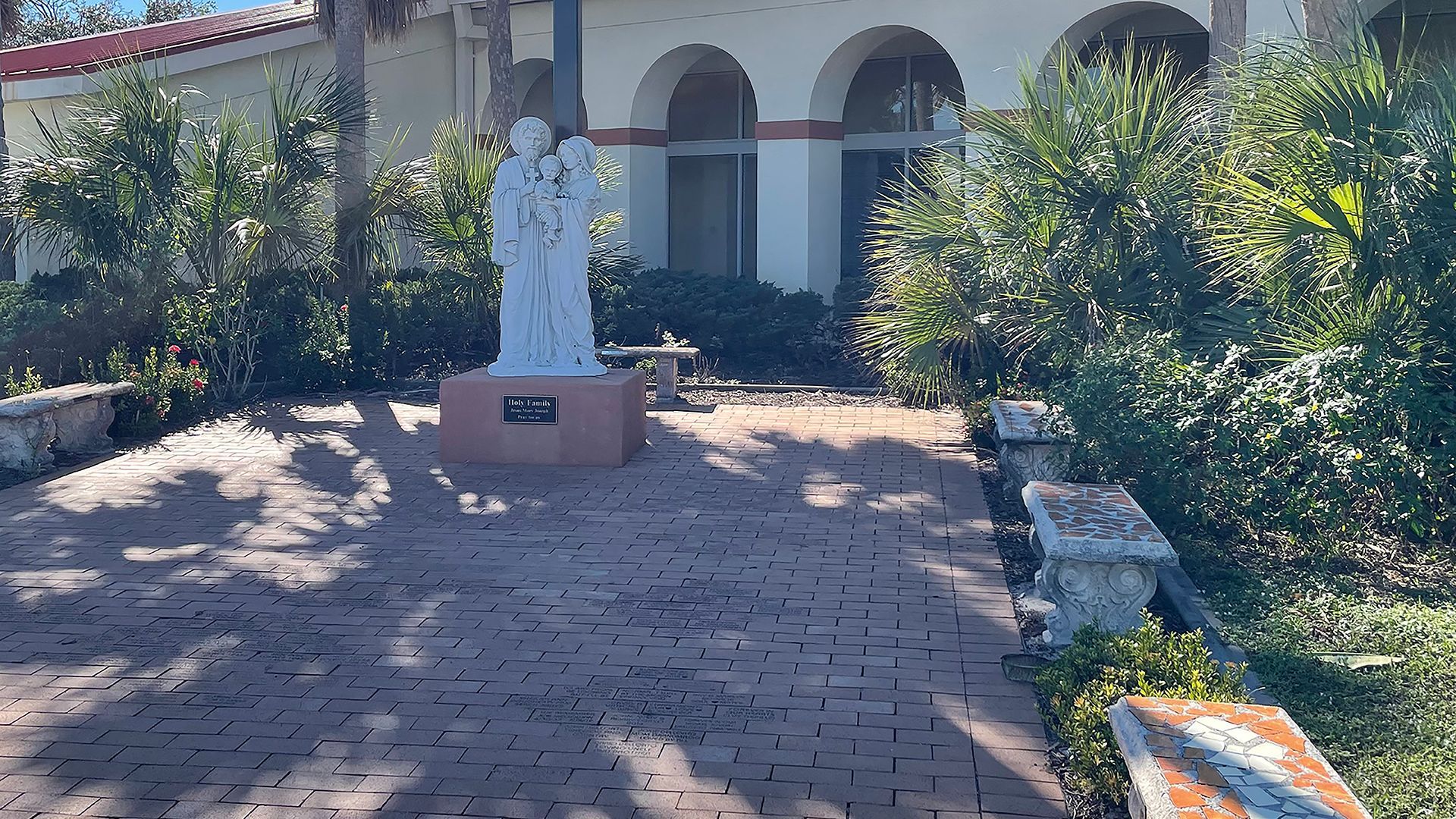 Courtyard with a white statue on a brick patio, surrounded by lush plants and arched house windows.
