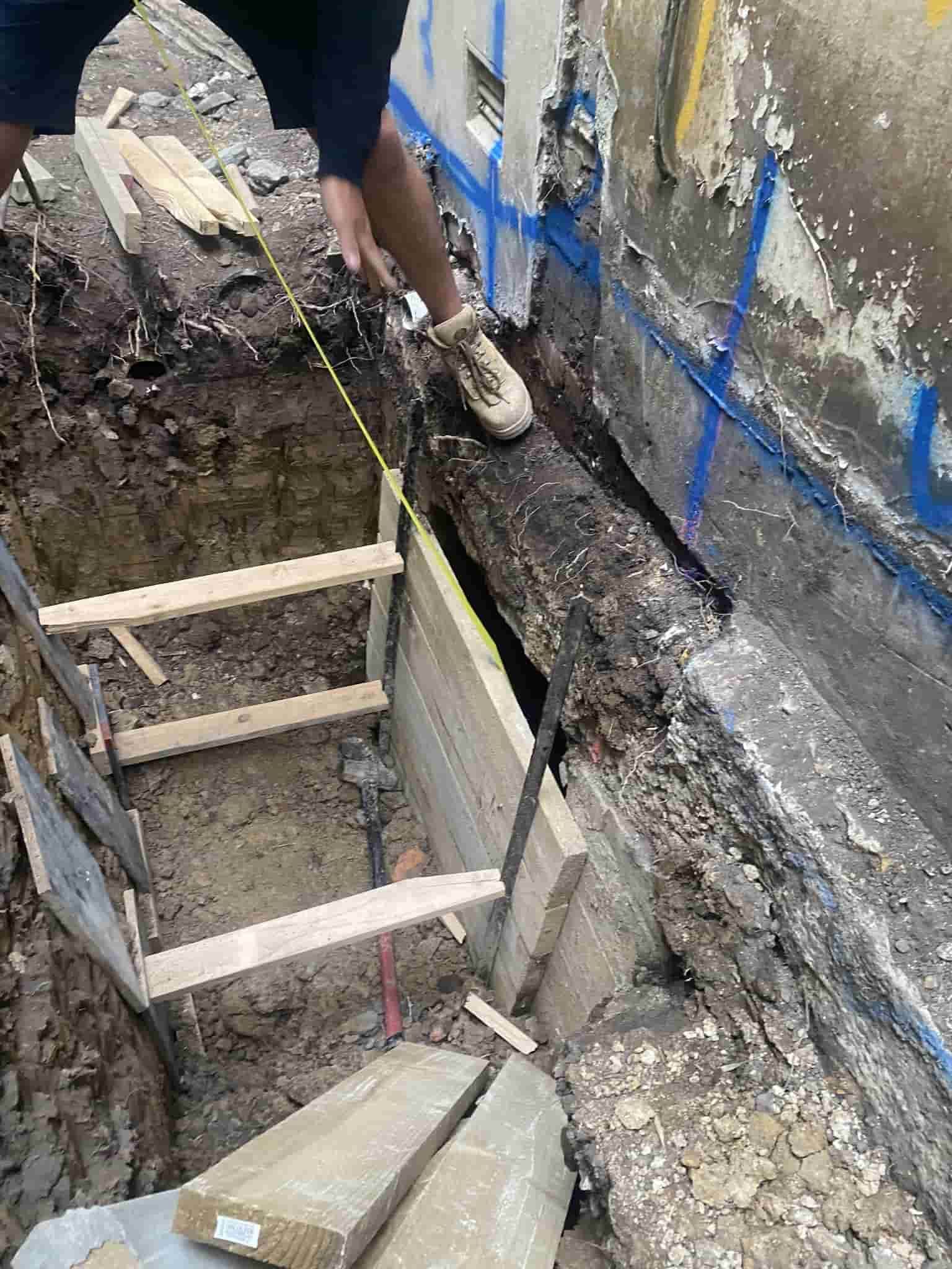 Person Measuring Inside a Trench. Wooden Bracing — Affordable Underpinning Solutions In Shell Cove, NSW