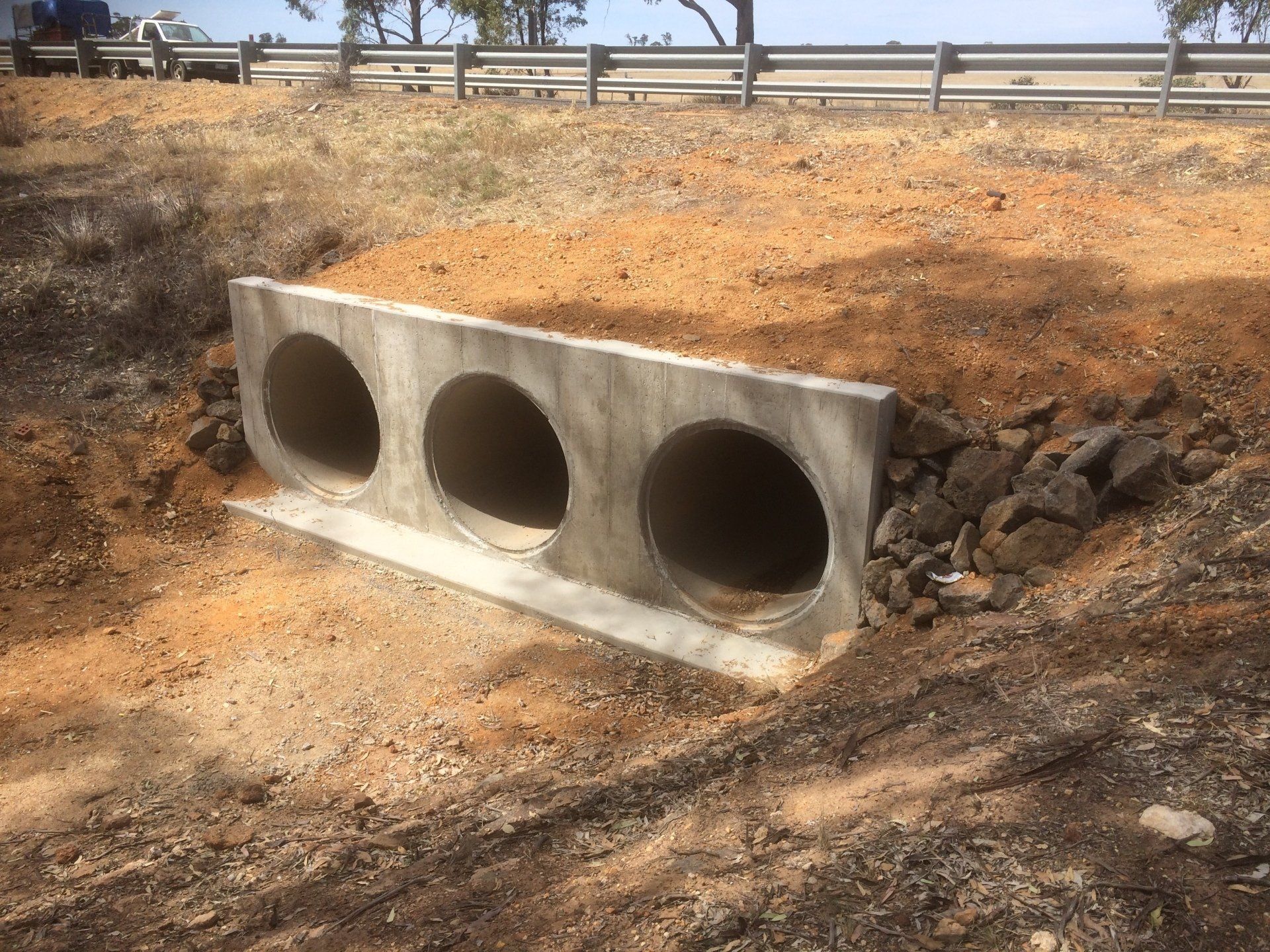 Three concrete culvert pipes installed in a dirt roadside drainage ditch