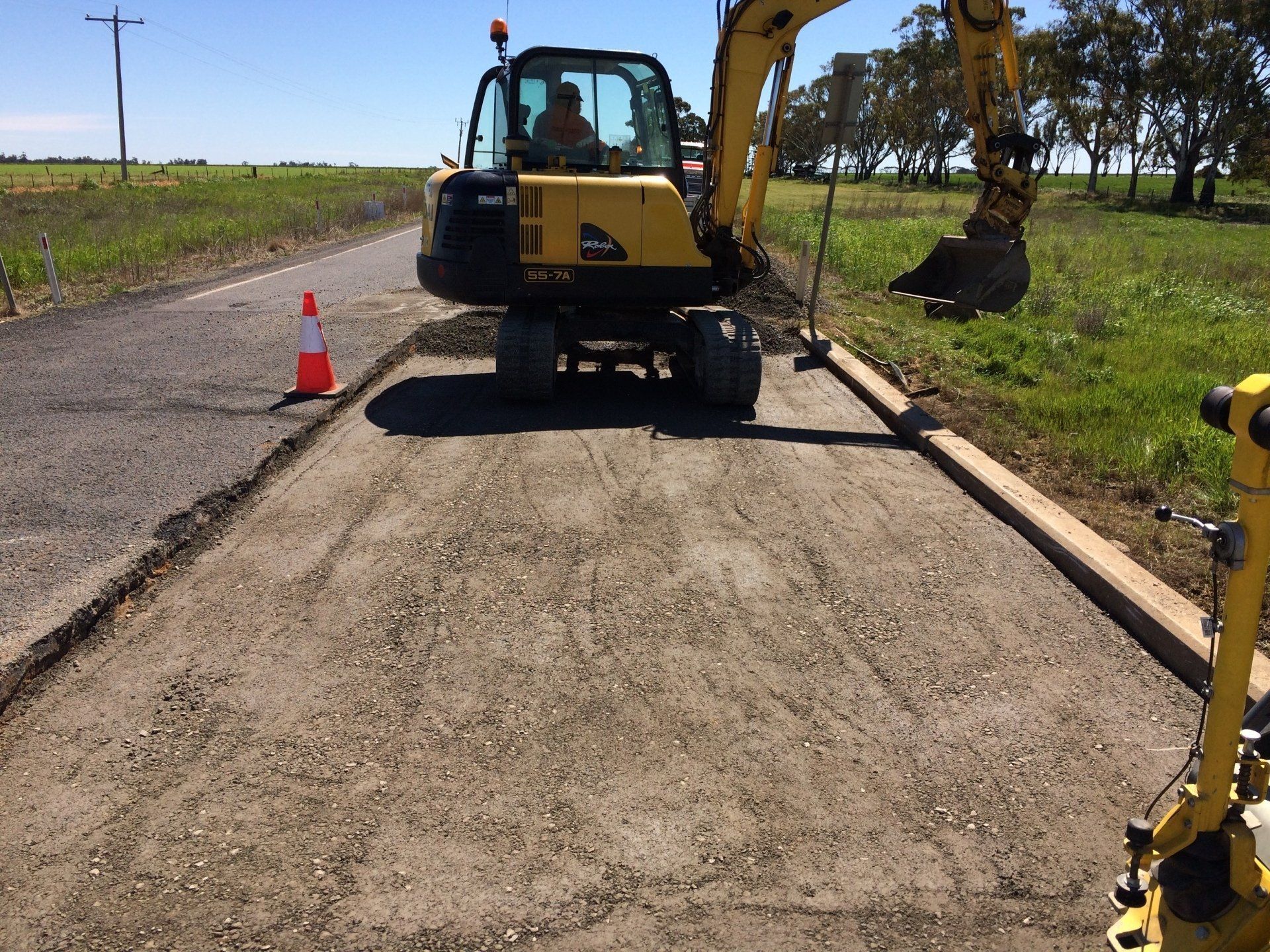 Construction equipment repairing a rural road with cones and gravel