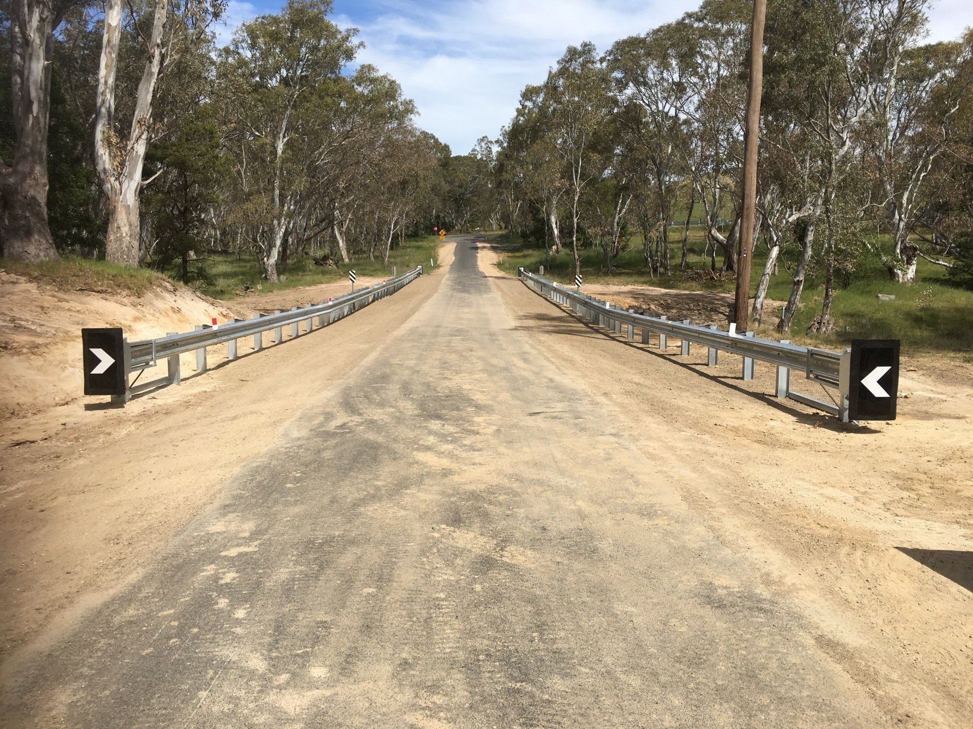 Dirt road bridge with metal guardrails crossing a dry, tree-lined area