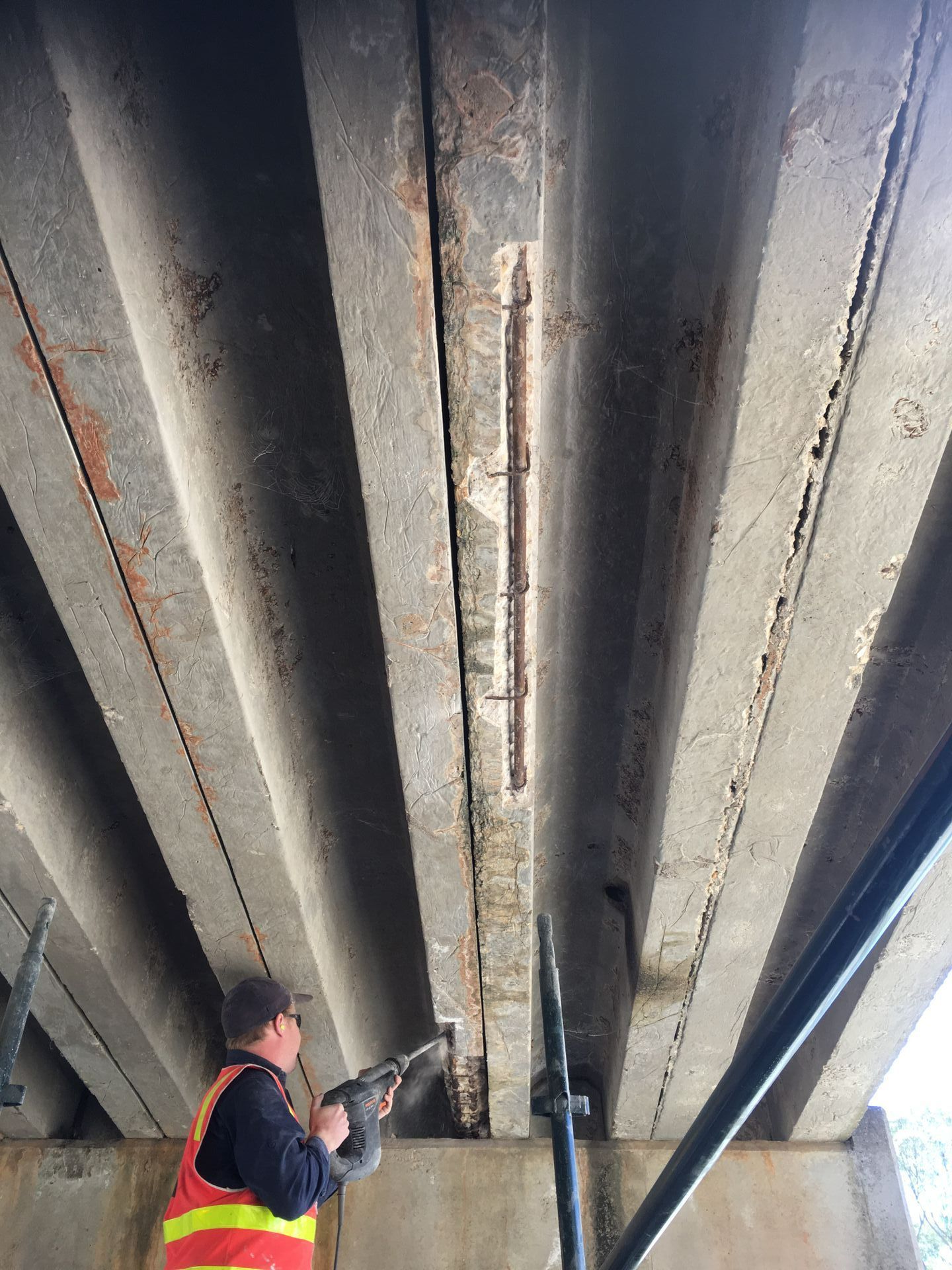 Worker inspecting the underside of a concrete bridge with a flashlight.