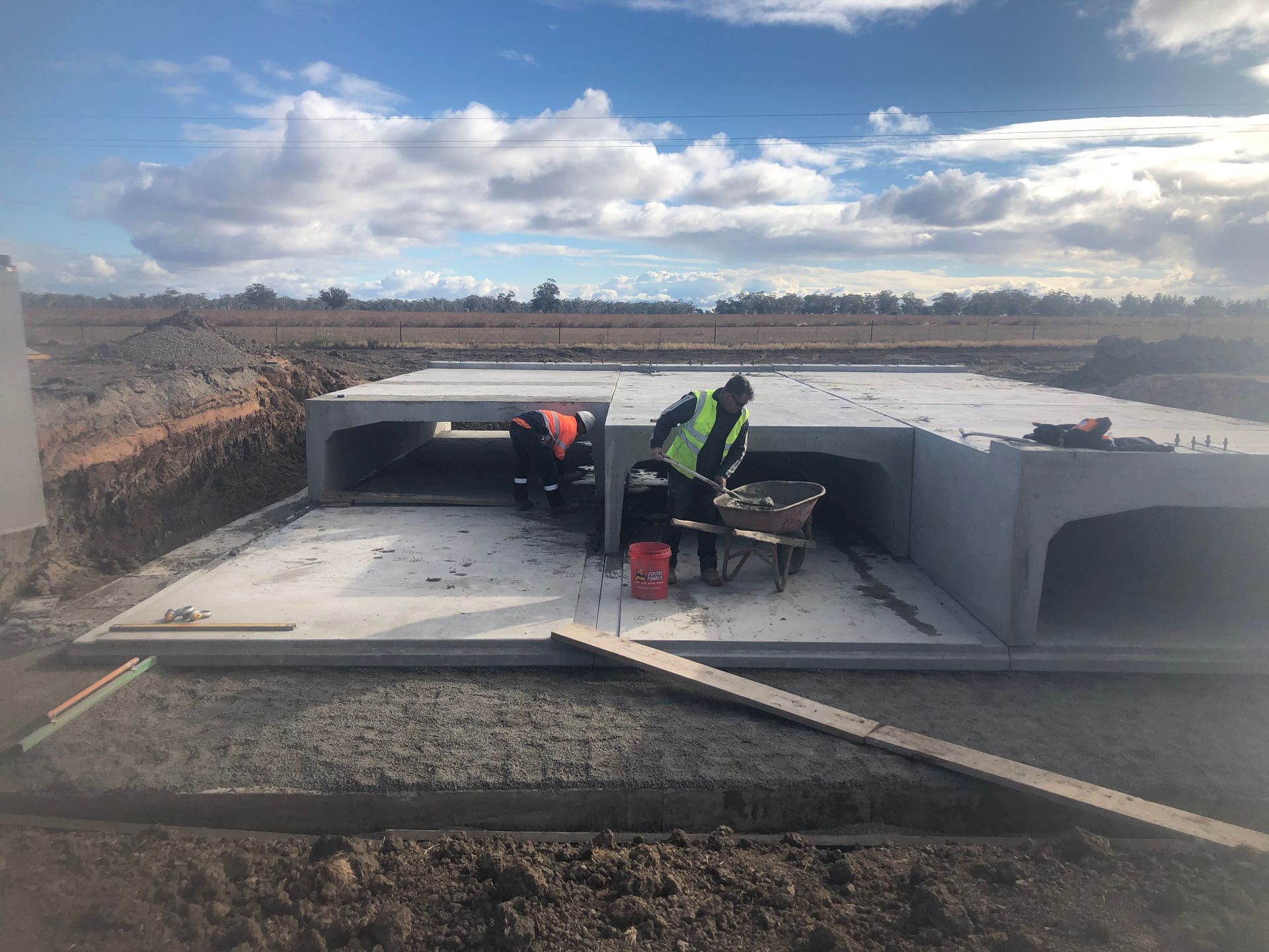 Workers installing a concrete foundation slab at a construction site under a cloudy sky