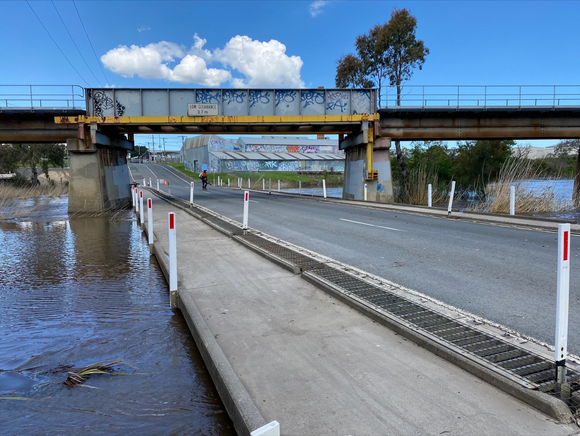 Flooded road under a bridge with water covering the left side and a wet, empty roadway on the right.