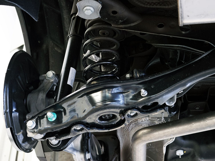 Close-up of a car’s front suspension and wheel assembly, showing coil spring, control arm, and brake components.