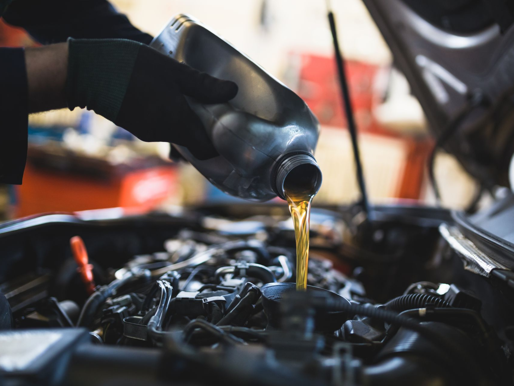 Gloved hand pouring motor oil into an engine