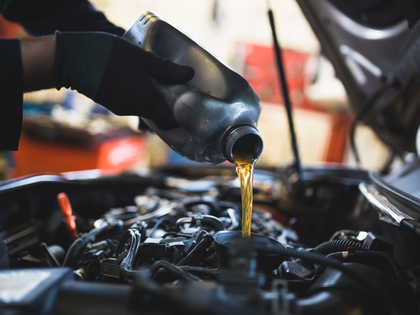 Oil pouring from a black bottle into a car engine during maintenance
