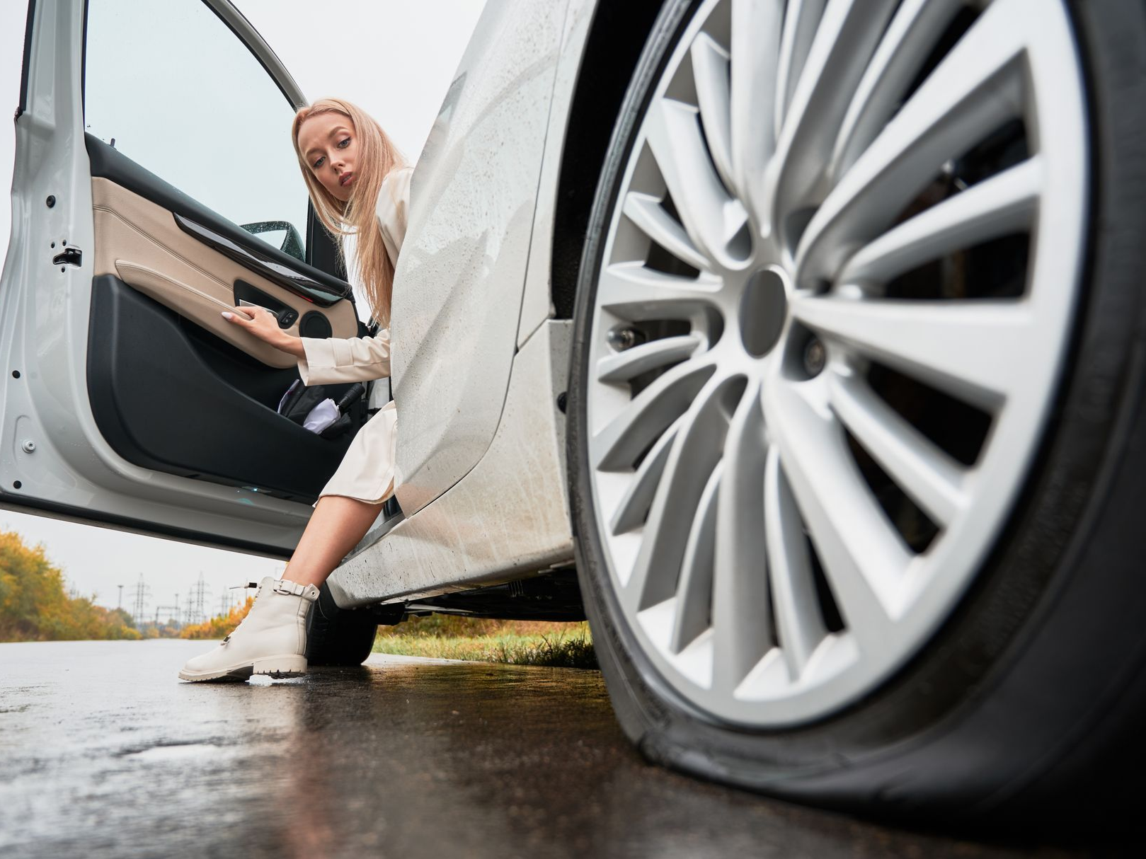 Woman stepping out of a car beside a close-up of the front wheel on a wet road