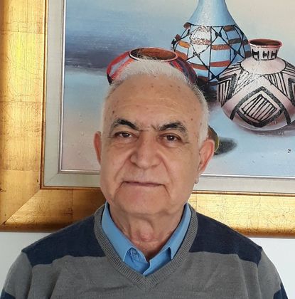 גבר קירח עם משקפיים מחייך, לובש חולצה שחורה עם צווארון וי.