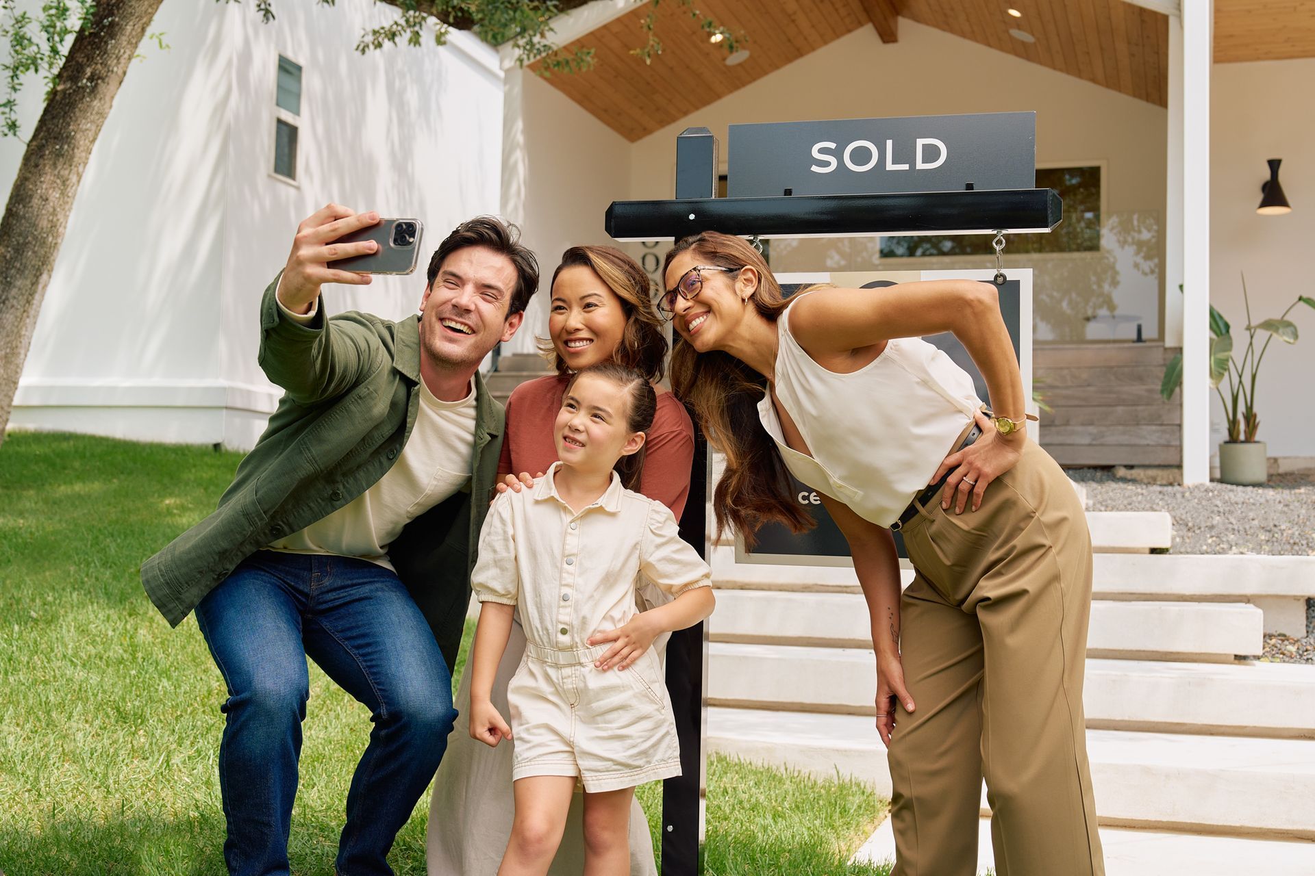Family taking a selfie in front of their new home with a sold sign