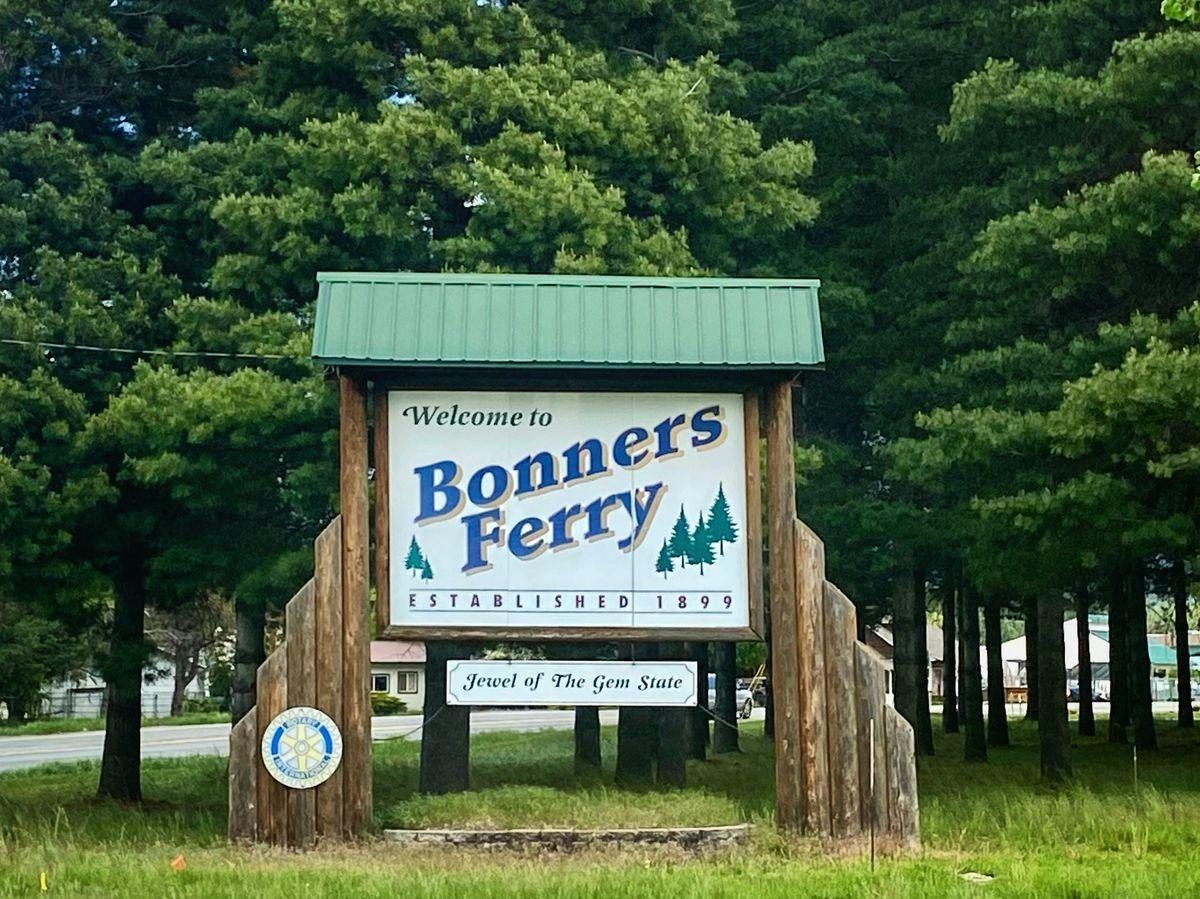 The Welcome to Bonners Ferry sign, established 1899, under tall pines in spring
