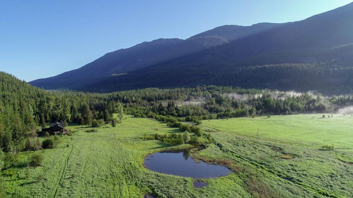 Aerial view of a small farm with a pond and pasture below forested mountains