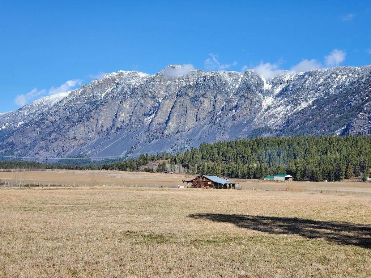 Fresh snow on the jagged Selkirk peaks above a brown valley pasture and a farmhouse in early March