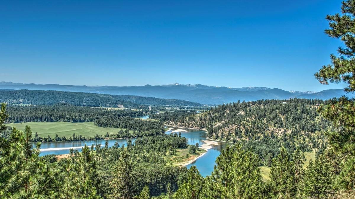 The Kootenai River bending blue through timber and farm ground with the Selkirk Mountains across the valley