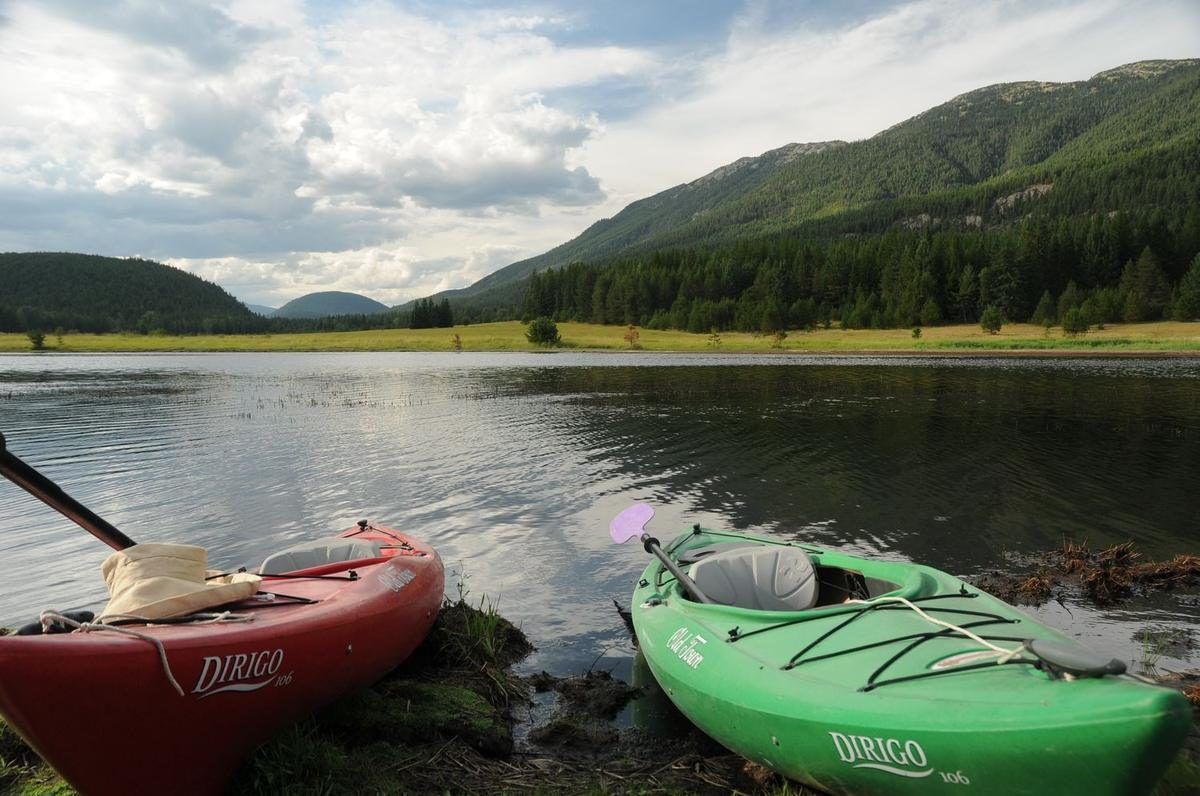 Two kayaks pulled up on the shore of a calm lake with mountains behind