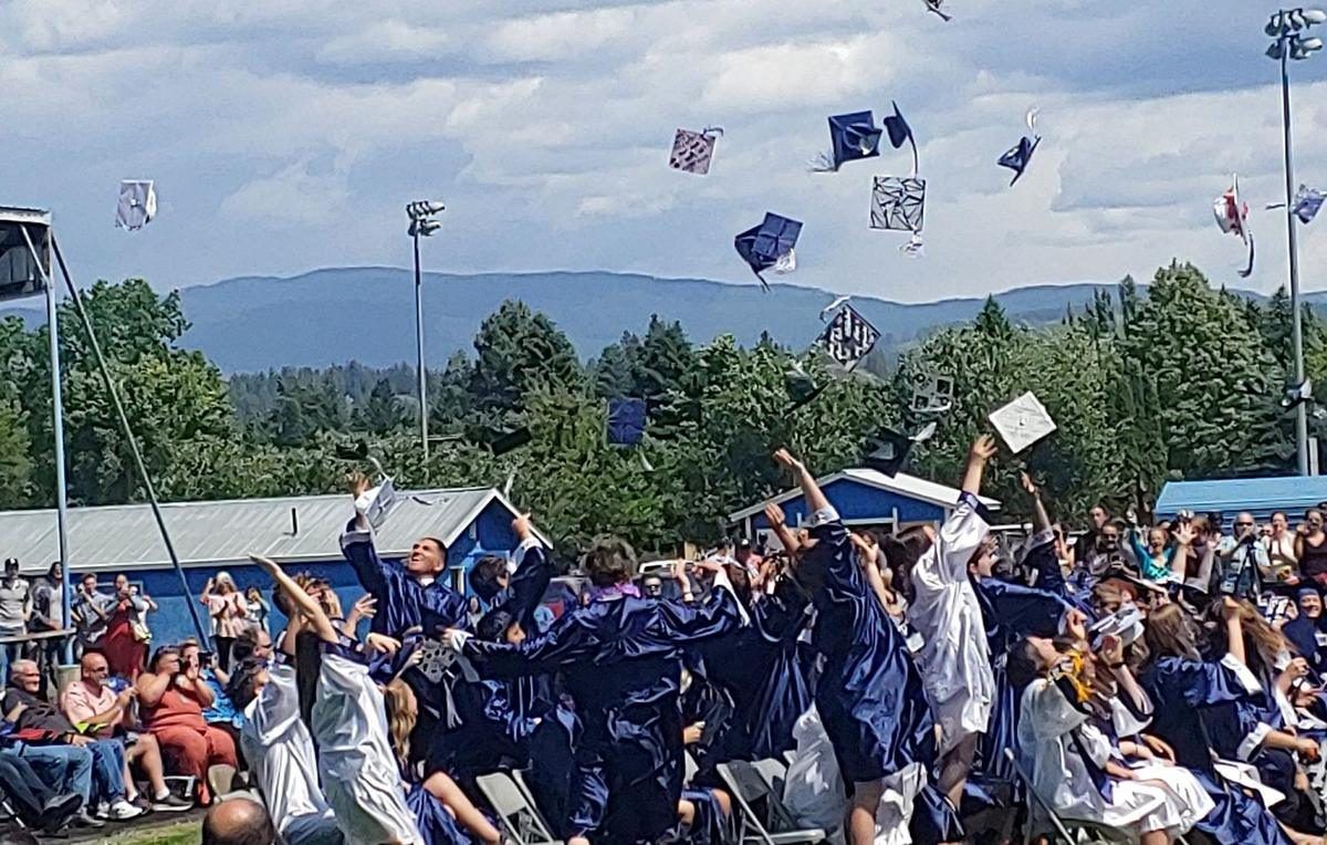 Bonners Ferry High School graduates throwing their caps in the air on the football field with the mountains behind