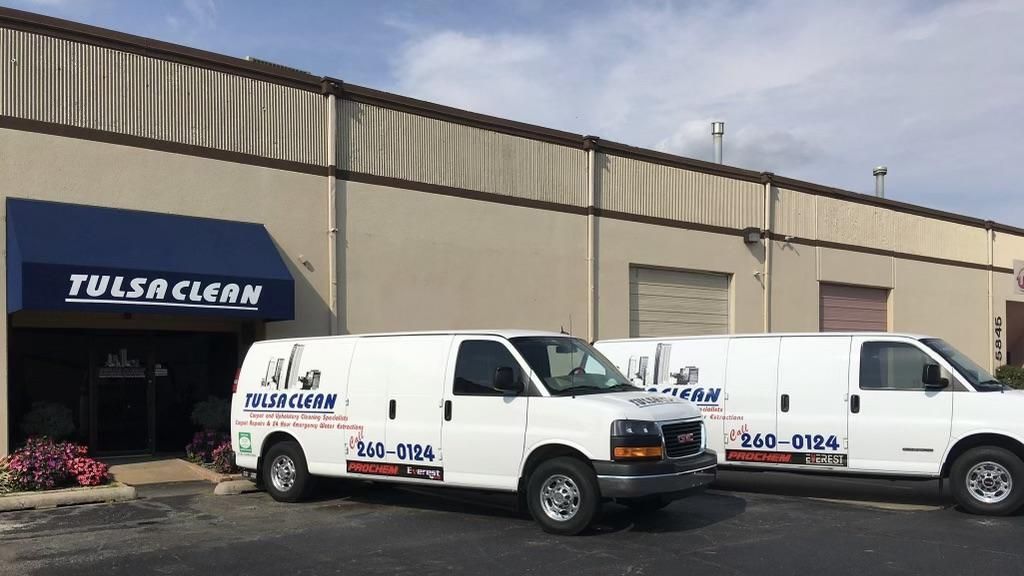 Two white vans are parked in front of a building that says tulsa clean