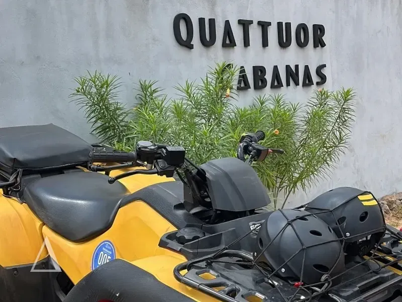 Close de um quadriciclo amarelo com dois capacetes pretos estacionado em frente à parede cinza com o logotipo