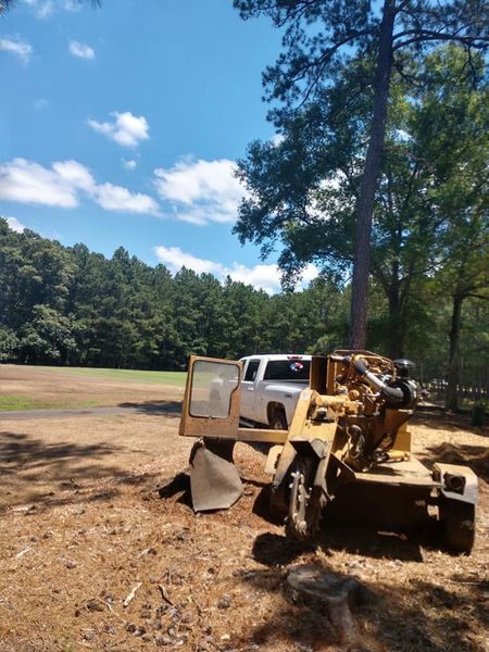 Yellow construction vehicle beside a white pickup on a dirt field under a blue sky