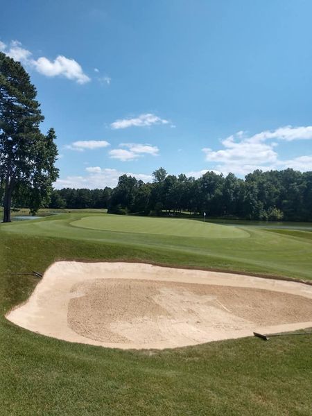 Golf course green with a sand bunker under a blue sky