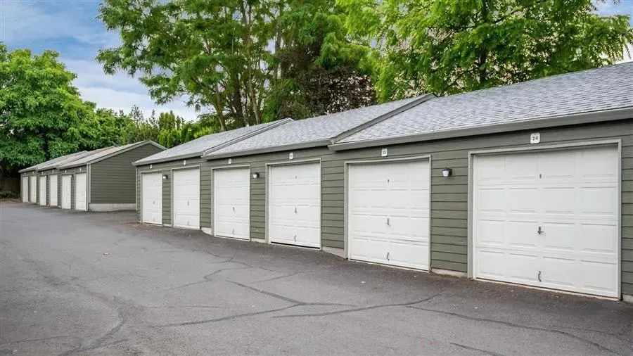 Row of gray storage unit garages with white doors and asphalt driveway.