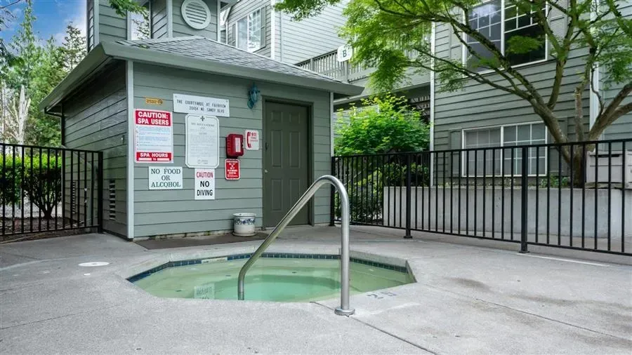 Hot tub surrounded by concrete, black fence, and small shed in front of a multi-story building.