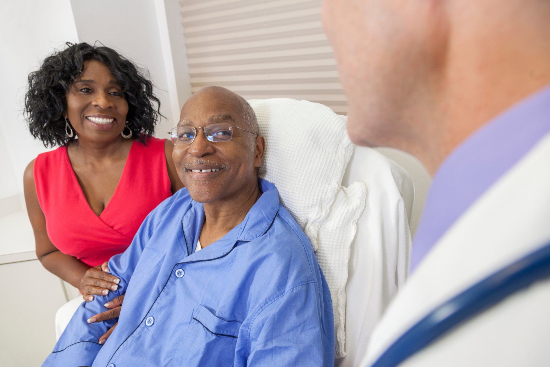 elderly man in hospital bed and elderly woman talking to doctor