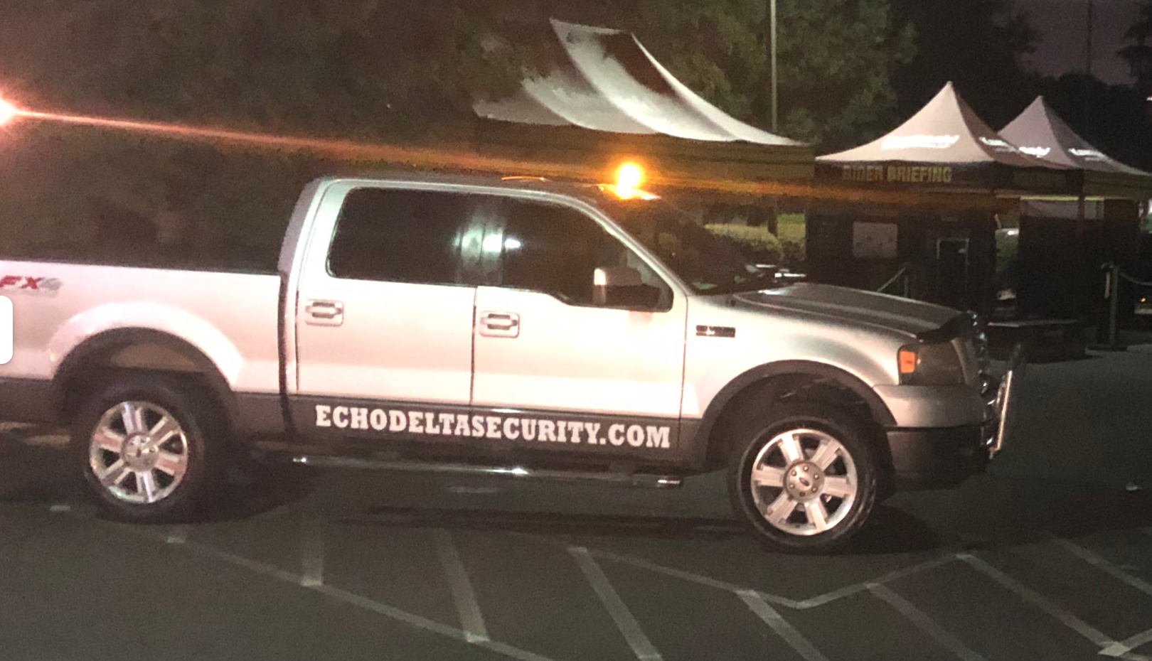 Silver security truck with flashing lights parked at an outdoor event, with