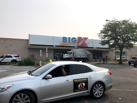Silver car in front of a Big Kmart with a garbage truck at the entrance. People stand nearby.