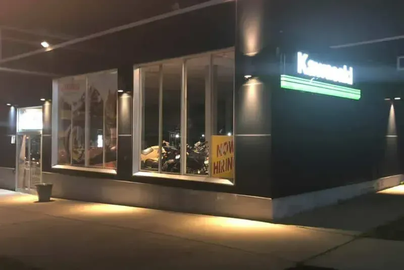 Exterior view of a Kawasaki motorcycle dealership at night; dark building with illuminated sign and display window.