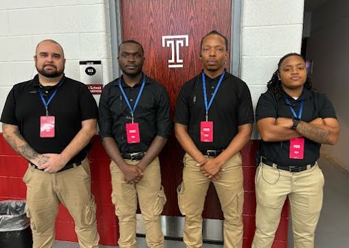 Four people in black shirts and khaki pants stand in front of a maroon door with a 