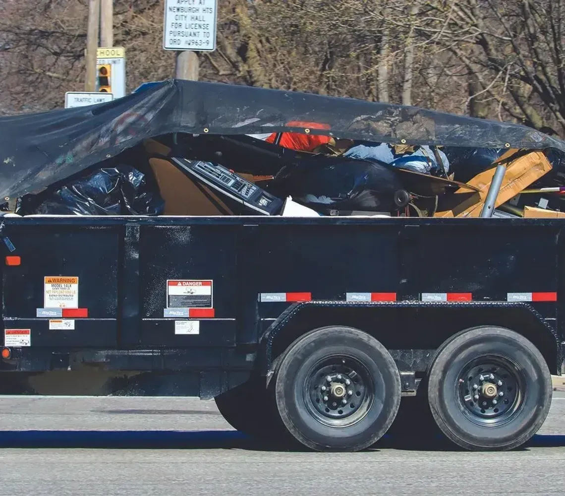 Loaded black dump trailer piled with debris, parked roadside in daylight