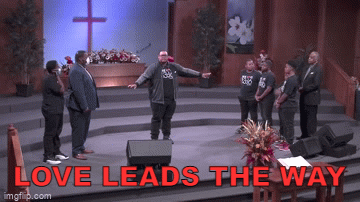 Man on stage with arms outstretched, leads group on stage in a church, text: 