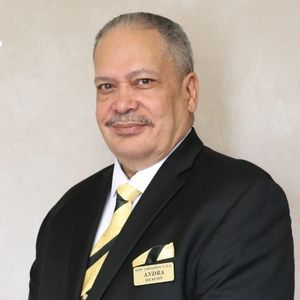 Man in black suit with yellow tie, smiling. Name tag reads