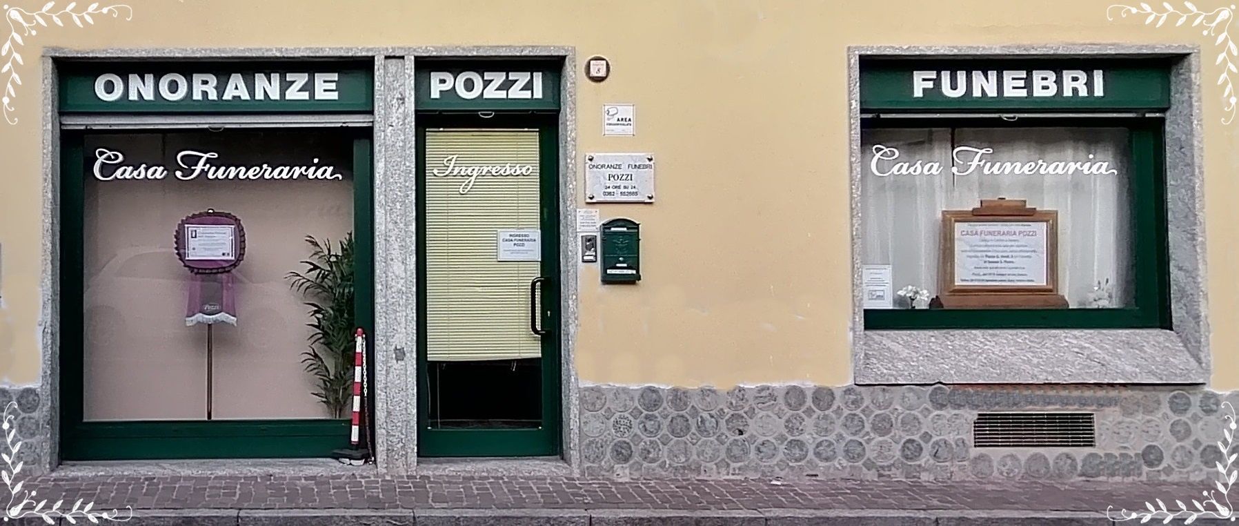 Vetrine con insegne nere e composizioni floreali, tra cui un ingresso centrale con la scritta