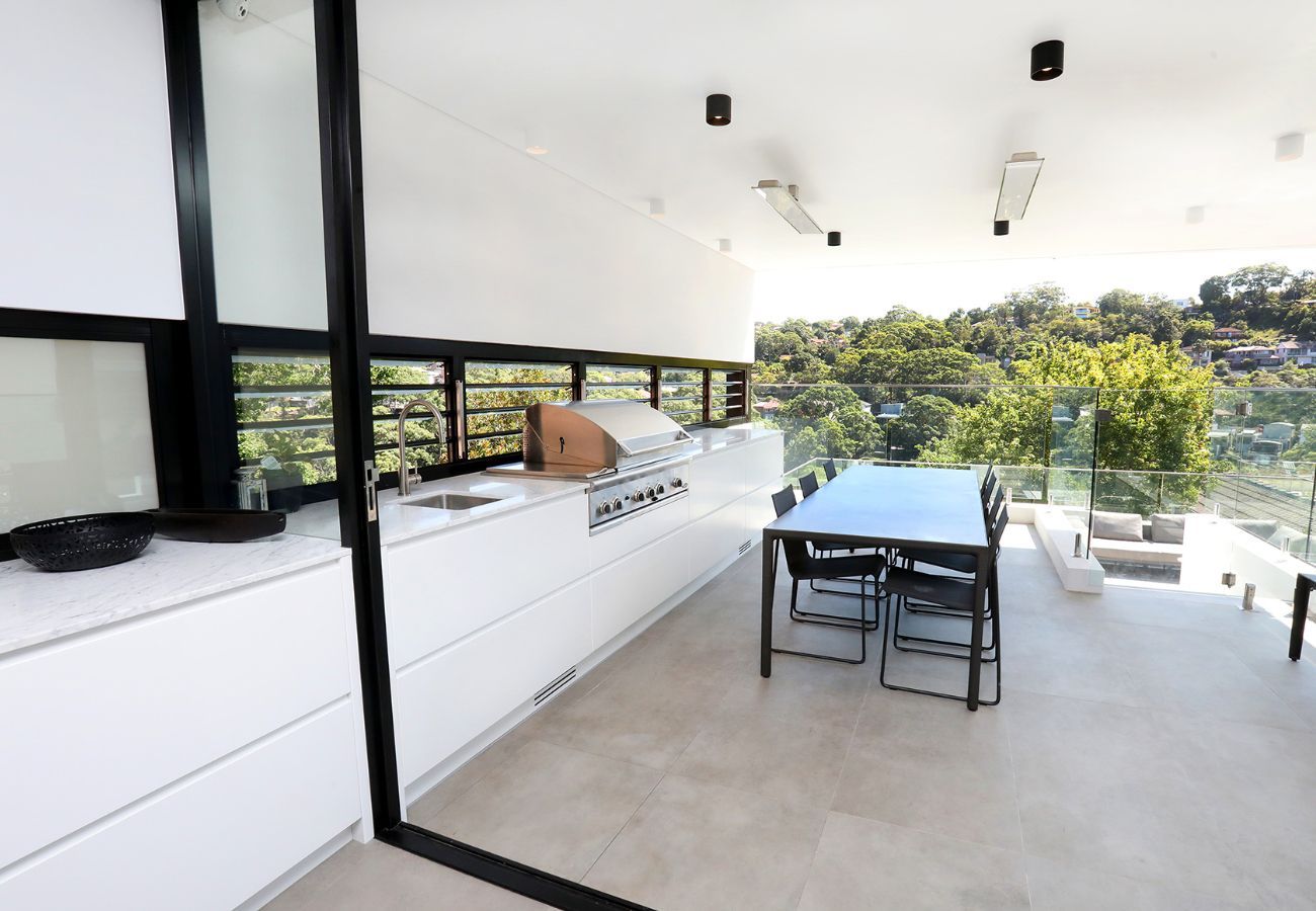 Outdoor Kitchen With Cabinets, Grill, and Dining Table Overlooking a Hillside — Affordable Tiles and Pavers In Morisset, NSW