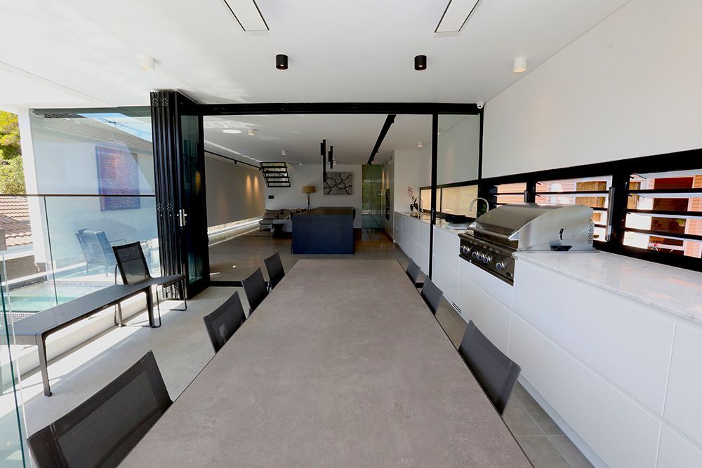 Outdoor Dining Area With a Long Table, Open to a Modern Kitchen and Pool Area — Affordable Tiles and Pavers In Morisset, NSW