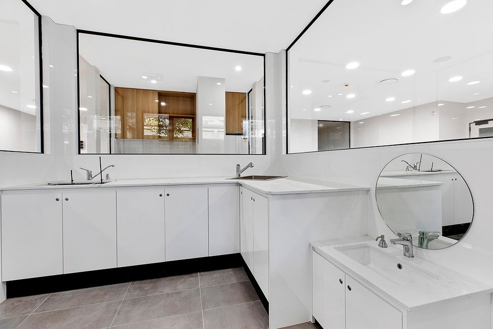 Modern White Kitchen With Sleek Cabinets, Large Window, and Round Mirror — Affordable Tiles and Pavers In Morisset, NSW