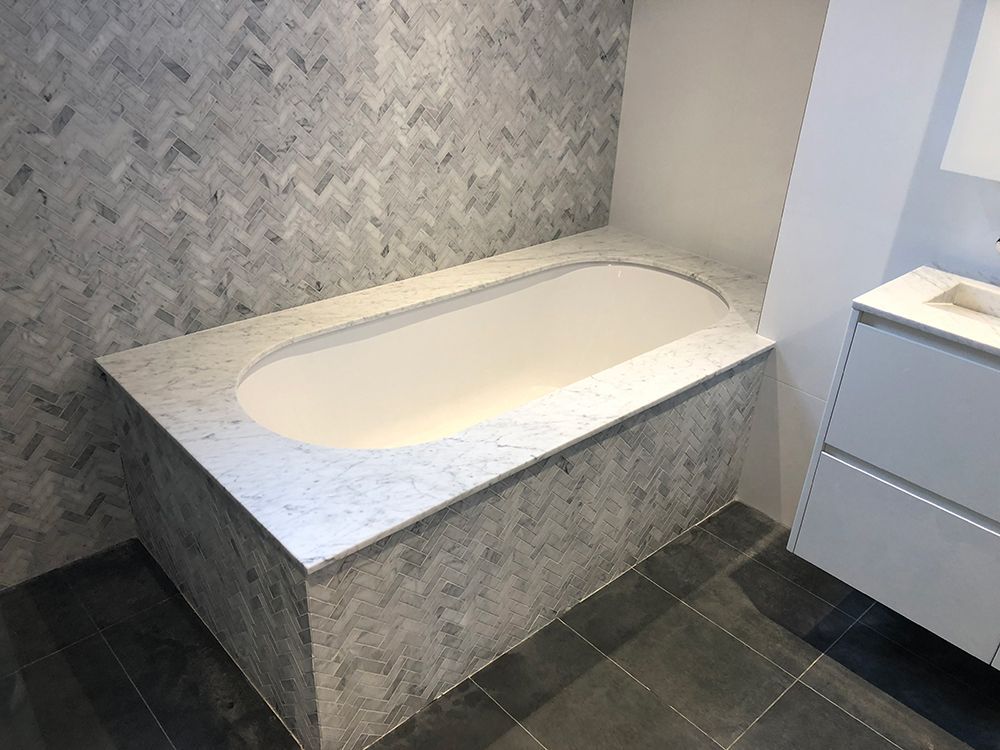 Bathroom With Herringbone Tile Wall, White Oval Tub, and Marble Tub Surround — Affordable Tiles and Pavers In Morisset, NSW