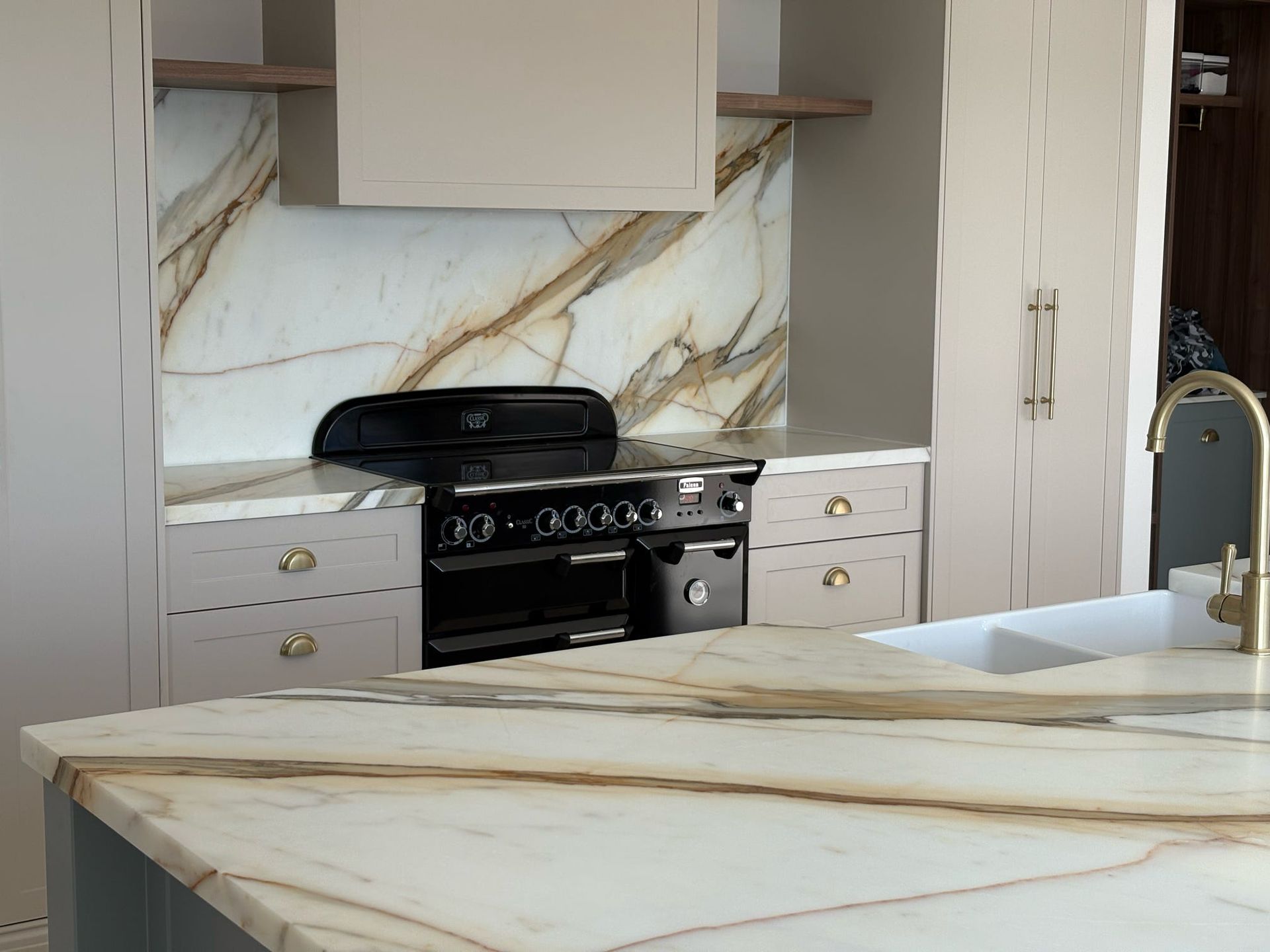 Modern kitchen with marble counters, white cabinetry, black stove, and gold faucet
