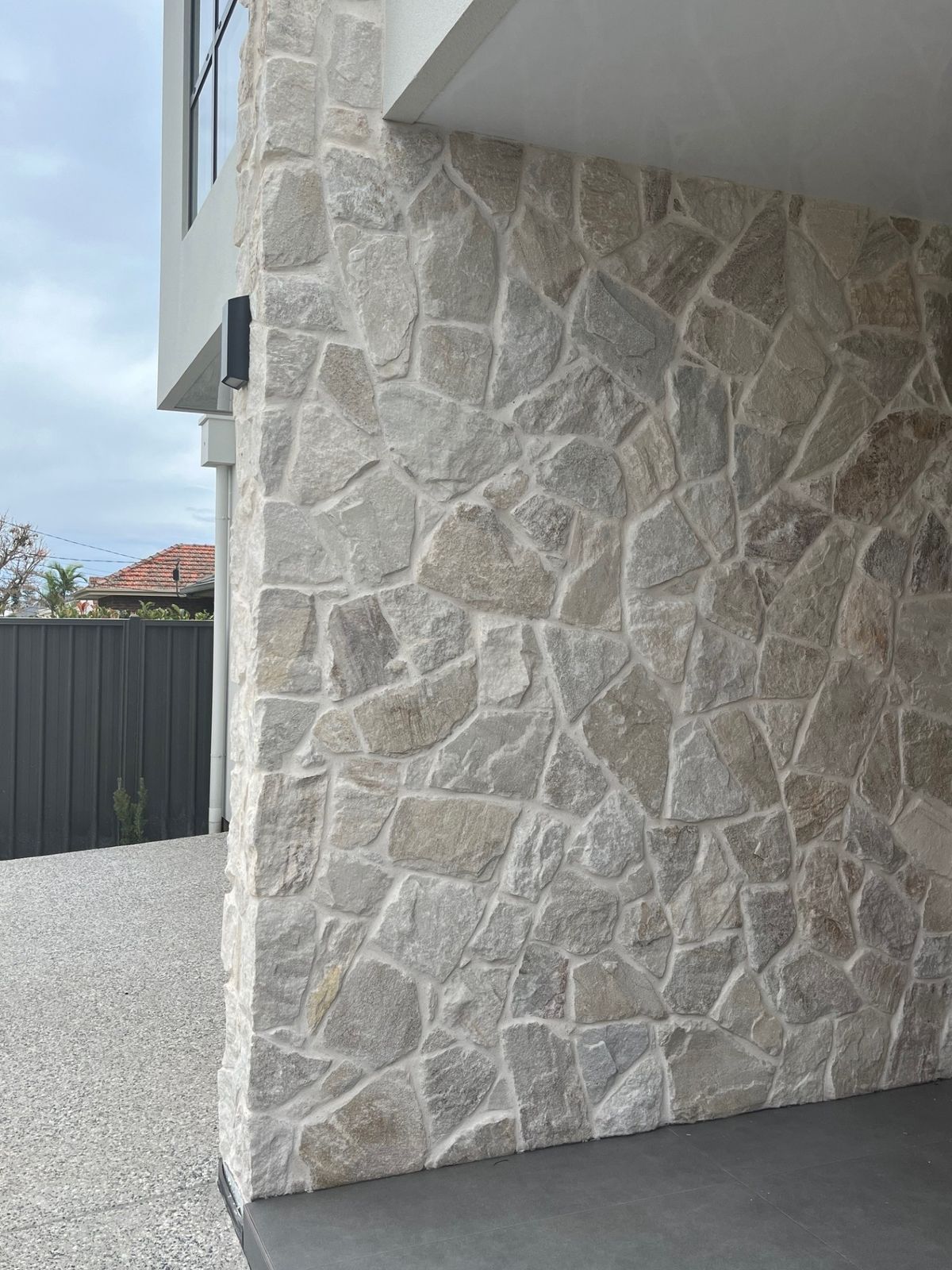 Stone-clad exterior corner of a modern building beside a paved driveway and black gate