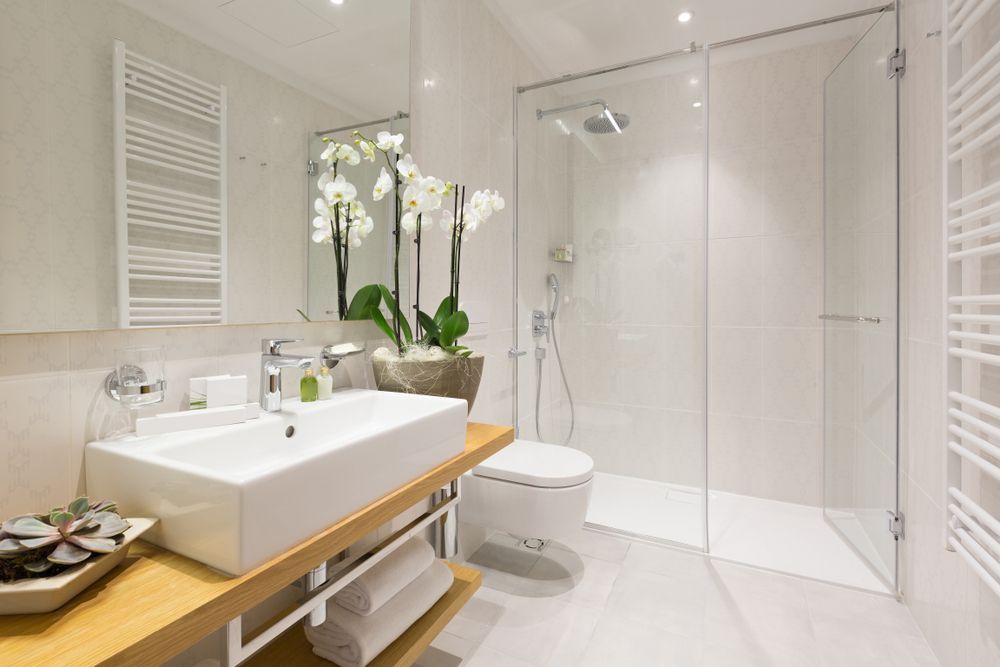 Modern White Bathroom With a Glass Shower, Sink, Toilet, and Orchids — Affordable Tiles and Pavers In Morisset, NSW