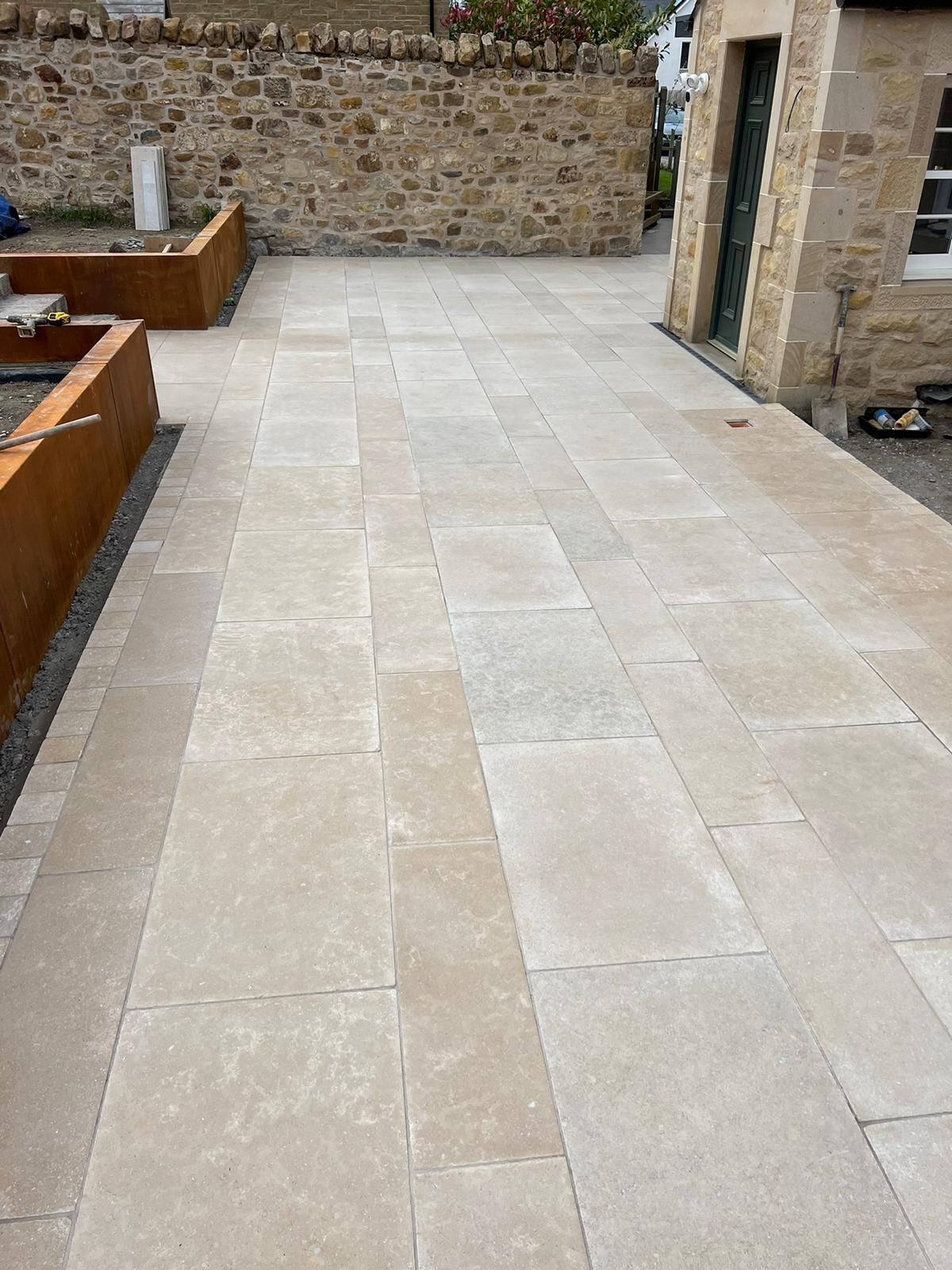 Stone patio with light beige paving slabs and a low stone wall in the background