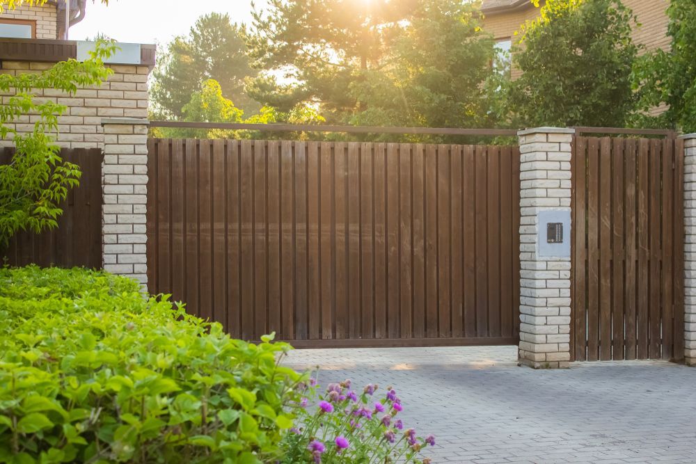 Wooden Driveway Gate With Brick Columns, Sunlight, and Green Foliage — Affordable Tiles and Pavers In Morisset, NSW