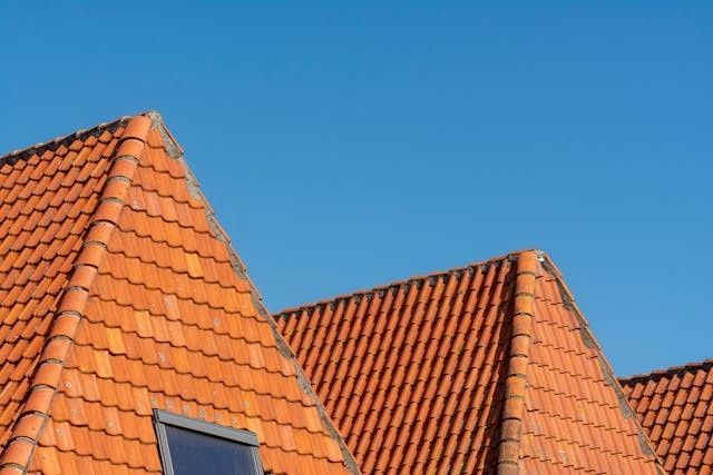 Orange clay tile roofing installed on residential homes under a clear blue sky.