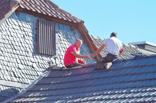 Roofing contractor repairing a red tile residential roof using scaffolding during a roof maintenance project.