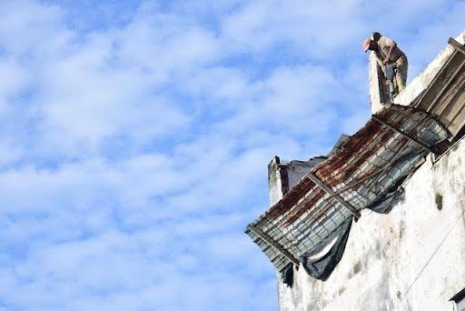 Workers repairing a damaged rooftop on a building under a blue sky during a roof restoration project