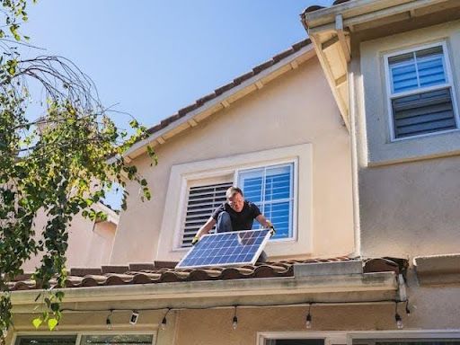 Worker installing a solar panel on a residential roof during home improvement and roofing maintenance work.