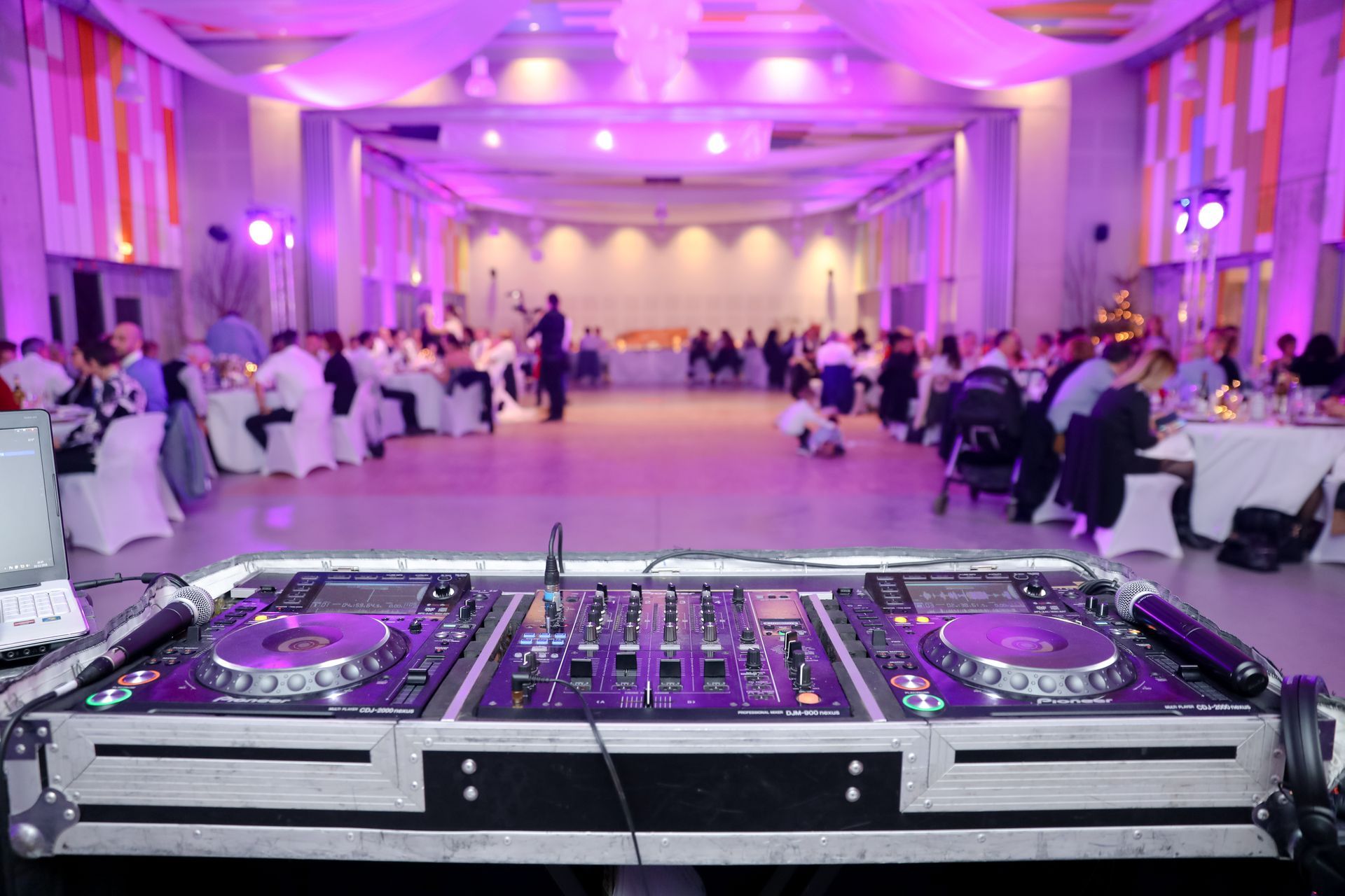 A dj is playing music in a large room at a wedding reception.