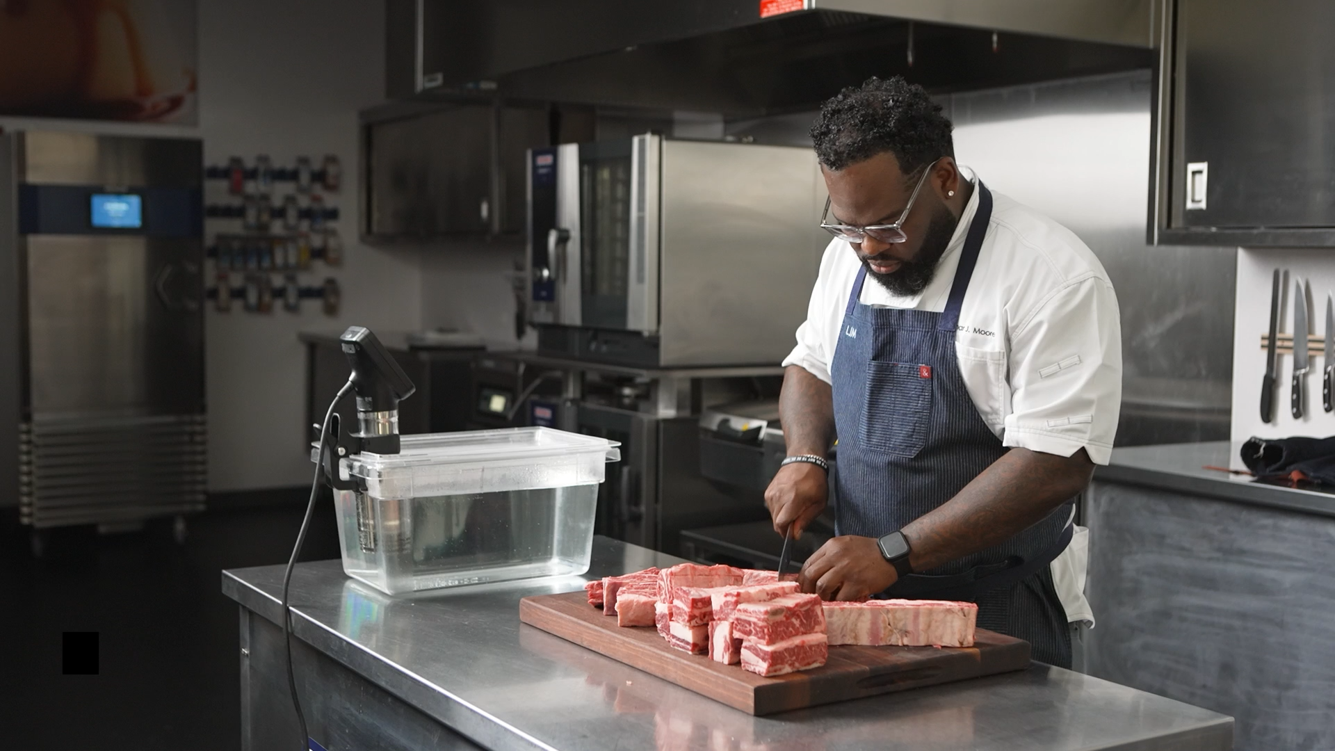 Chef Lamar Moore preparing bone-in short ribs for vacuum sealing and sous vide cooking in a professional kitchen.
